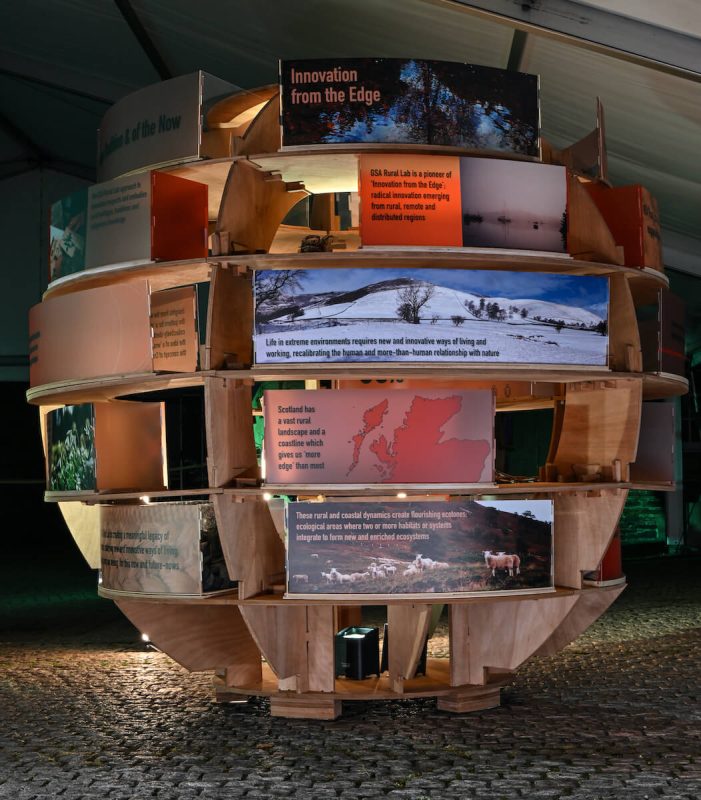 Darkened exhibition space featuring circular timber display with pink and orange illuminated panels.
